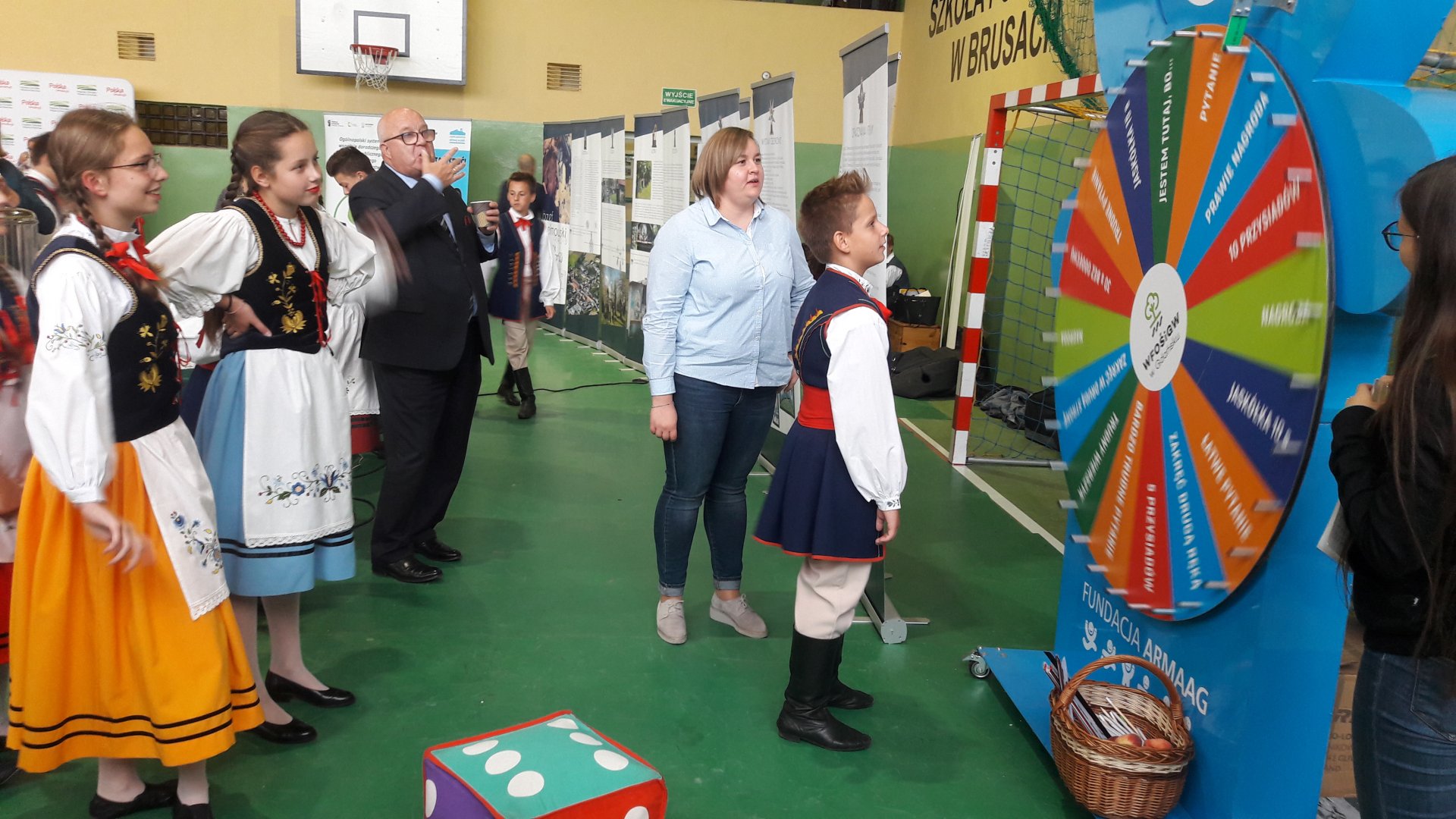 Stanowisko Wojewódzkiego Funduszu Ochrony Środowiska i Gospodarki Wodnej w Gdańsku podczas Pomorskiego Kongresu Kół Gospodyń Wiejskich w Brusach, na zdjęciu koło fortuny, obok stoi pracownik Funduszu, dookoła uczestnicy kongresu