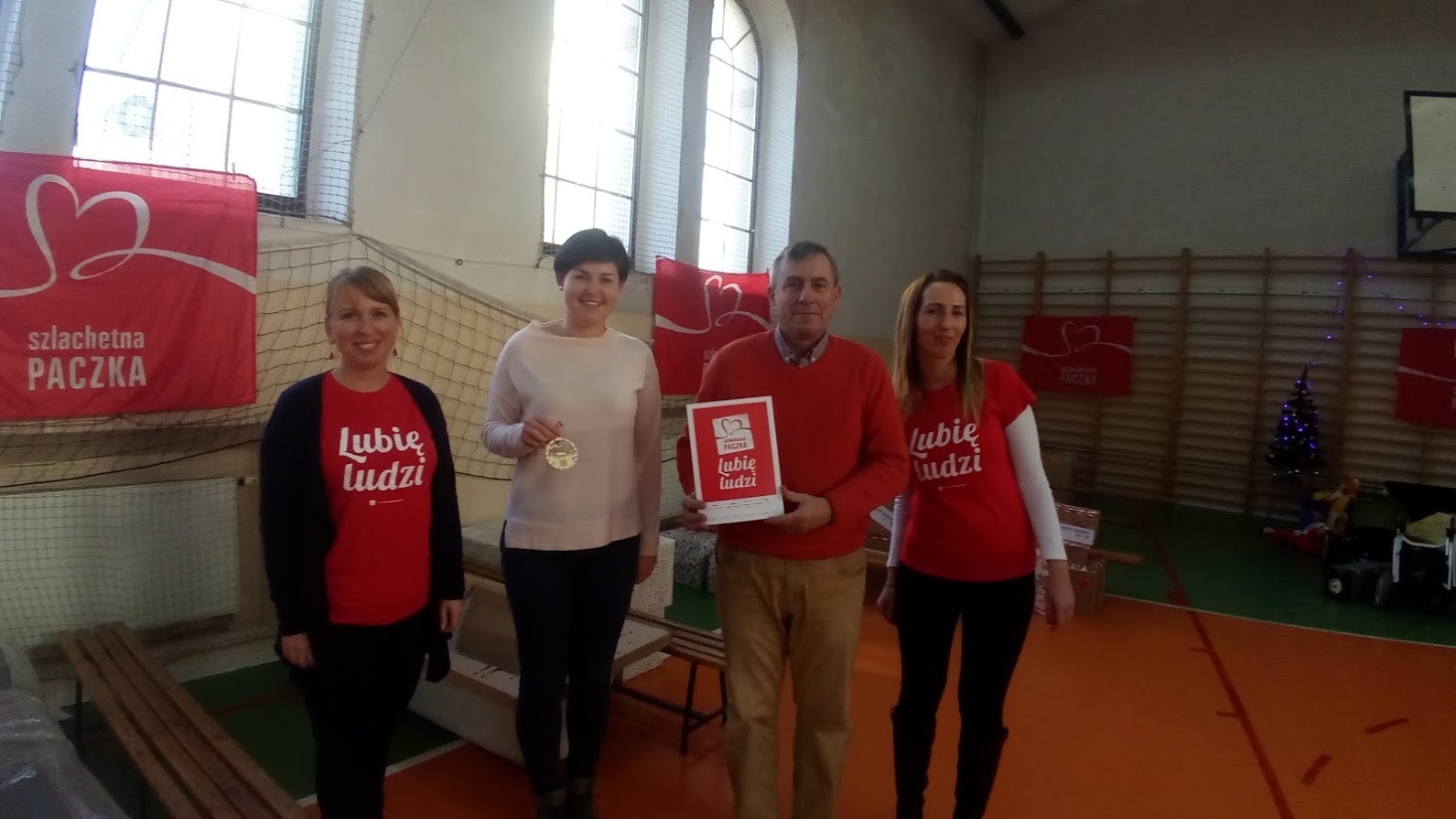 Sala magazynu Szlachetnej Paczki w Kwidzynie; na środku stoją cztery osoby osoby: dwoje pracowników WFOSiGW w Gdańsku oraz dwie wolontariuszki Szlachetnej Paczki