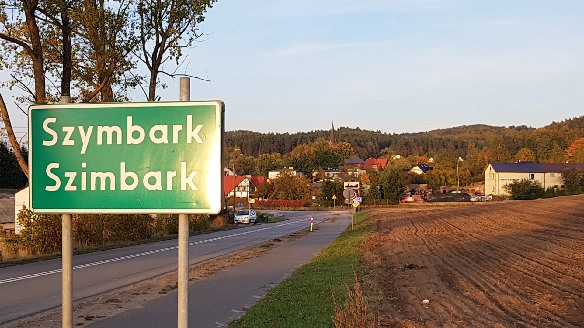 Miejscowośc Szymbark w gminie Stężyca, na zdjęciu znak drogowy z napisem „Szymbark”, droga, domy.