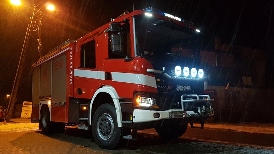 Czerwony samochód ratowniczo-gaśniczy OSP Pręgowo z włączonymi światłami, zdjęcie wykonane w nocy