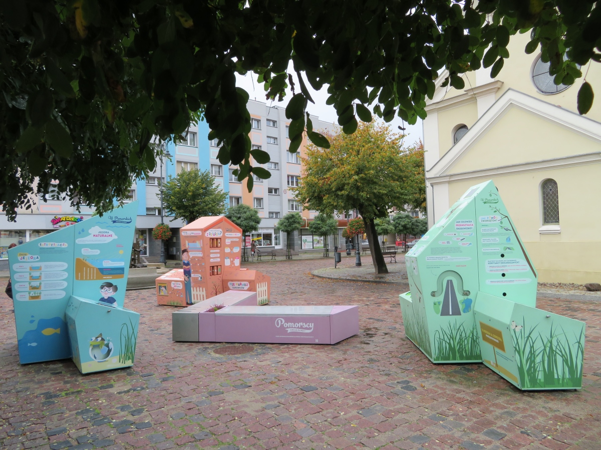 Na zdjęciu trzy bryły oraz ławka tworzące interaktywną wystawę plenerową