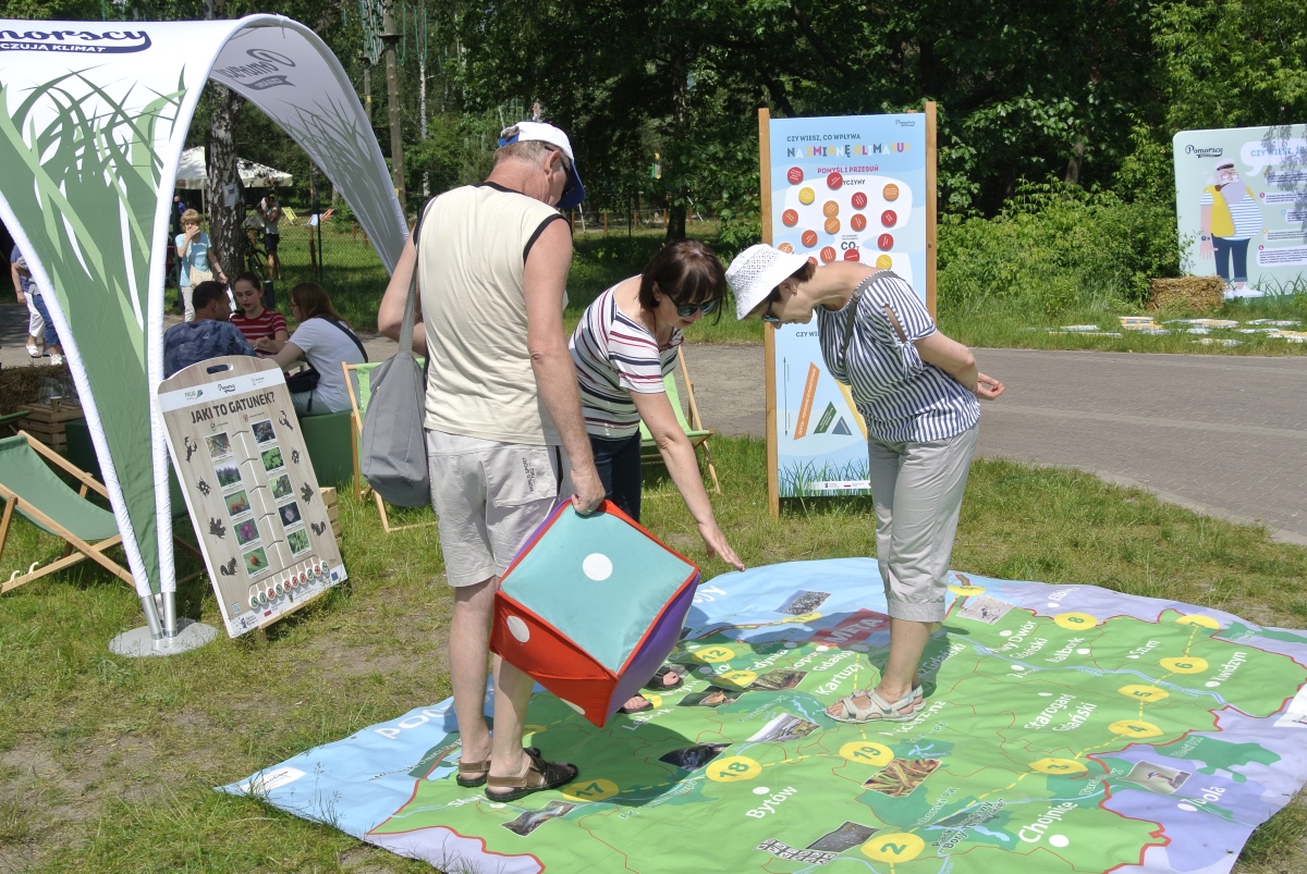 Trzy osoby stoją na planszy gry wielkoformatowej rozłożonej na trawniku