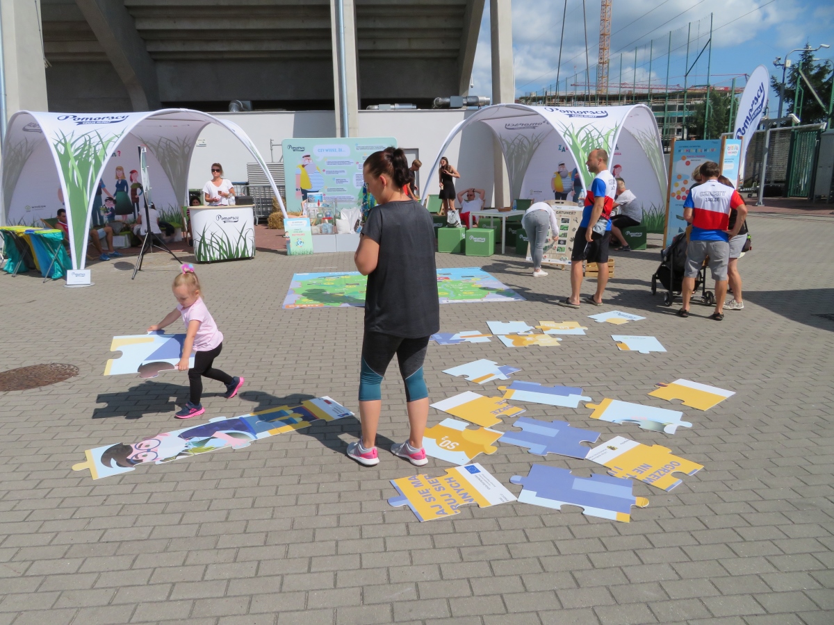 Na zdjęciu widać dwa kolorowe namioty Rodziny Pomorskich, na środku dziewczynka z mamą układa edukacyjne puzzle;