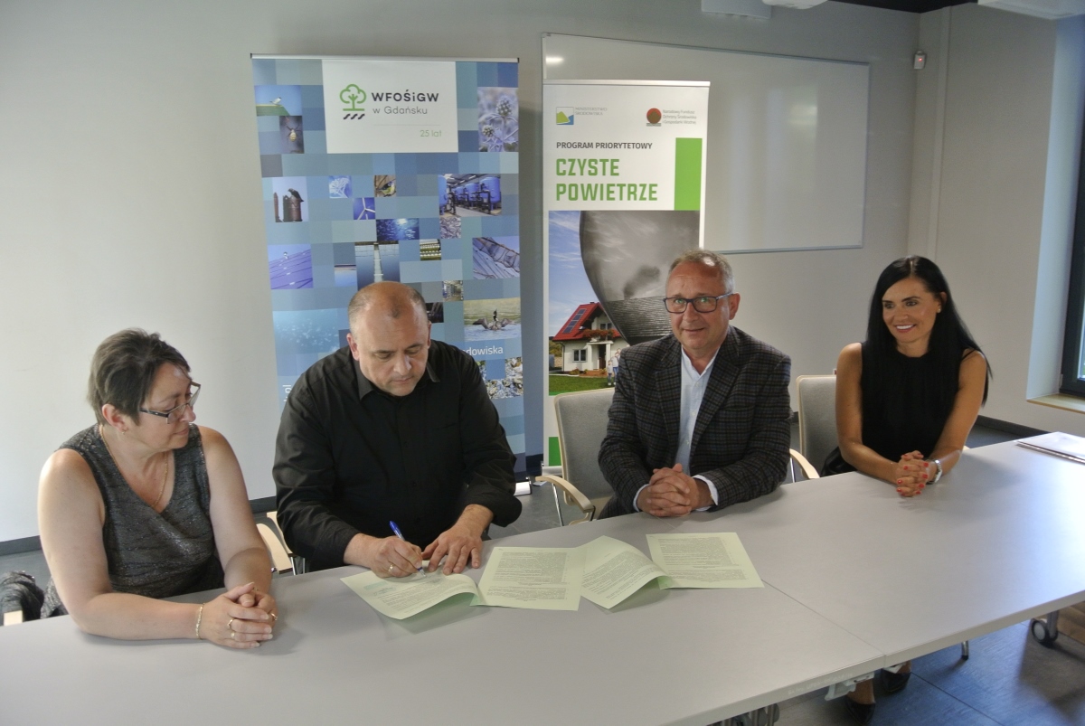 Przy stole siedzą cztery osoby i podpisują tysięczną umowę w ramach „Czystego Powietrza
