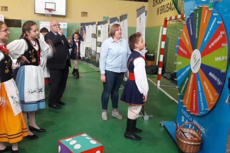 Stanowisko Wojewódzkiego Funduszu Ochrony Środowiska i Gospodarki Wodnej w Gdańsku podczas Pomorskiego Kongresu Kół Gospodyń Wiejskich w Brusach, na zdjęciu koło fortuny, obok stoi pracownik Funduszu, dookoła uczestnicy kongresu