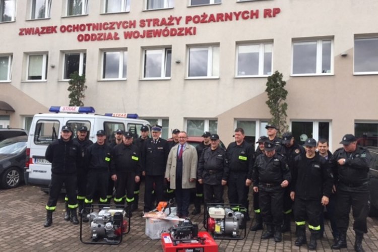 Prezes WFOŚiGW w Gdańsku Maciej Kazienko wraz ze strażakami OSP województwa pomorskiego. Na ziemi leży  specjalistyczny sprzęt dla strażaków.