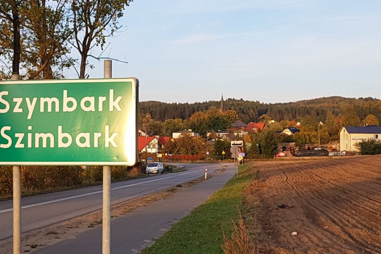 Miejscowośc Szymbark w gminie Stężyca, na zdjęciu znak drogowy z napisem „Szymbark”, droga, domy.