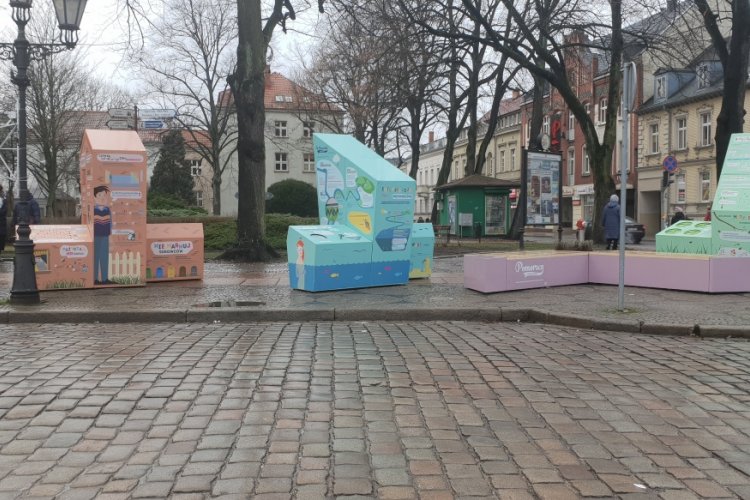Interaktywna wystawa plenerowa, składająca się z trzech brył i ławki, na placu w Słupsku