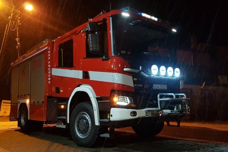 Czerwony samochód ratowniczo-gaśniczy OSP Pręgowo z włączonymi światłami, zdjęcie wykonane w nocy