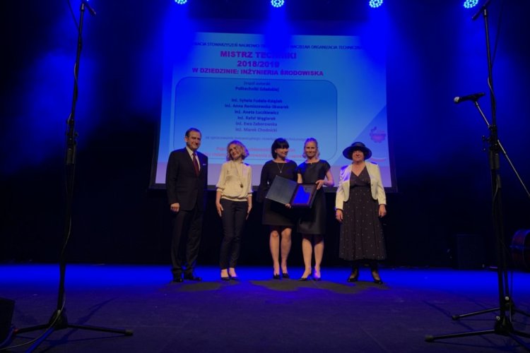 Na scenie stoi pięć osób (cztery kobiety, jeden mężczyzna), jedna z nich trzyma w rękach certyfikat. Za ich plecami slajd z napisem „Mistrz techniki w dziedzinie Inżynierii Środowiska”.