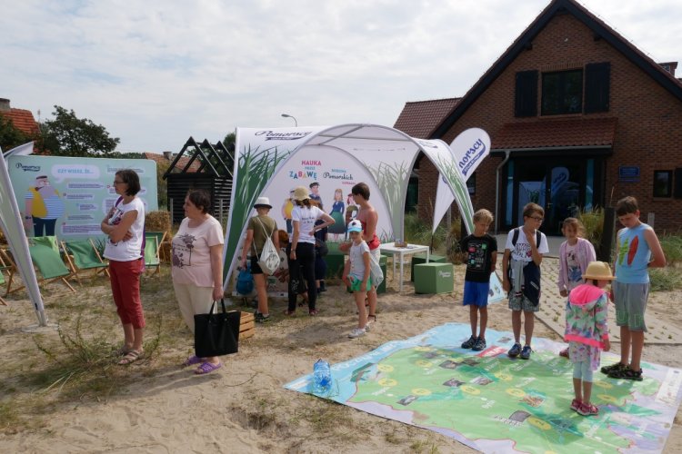 Edukacyjne stoisko Rodziny Pomorskich podczas Dnia Ryby w Helu; na zdjęciu widać namiot, na ziemi leżą rozłożone puzzle, dookoła dużo dzieci i dorosłych