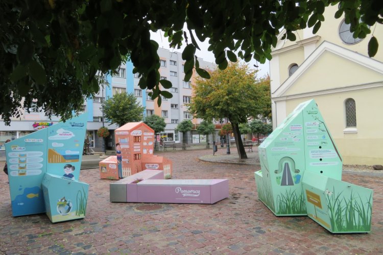 Na zdjęciu trzy bryły oraz ławka tworzące interaktywną wystawę plenerową