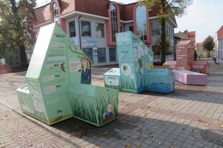 Trzy bryły tworzące interaktywną wystawę plenerową na placu, za nimi budynek