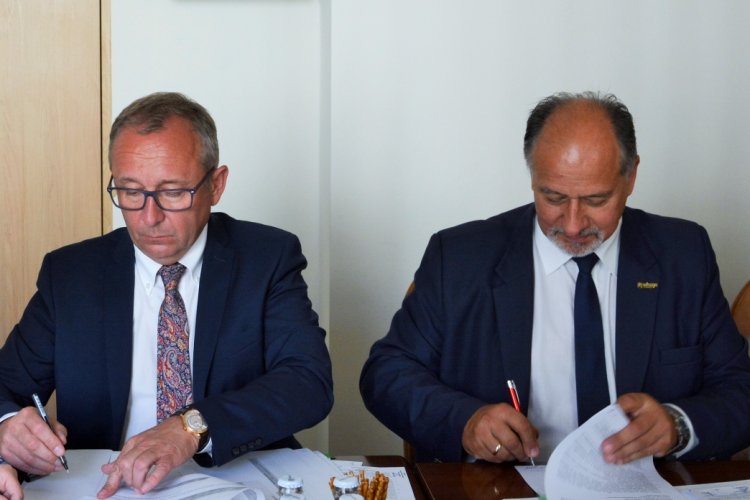 Przy stole siedzi dwóch mężczyzn, podpisują umowy. Jednym z nich jest prezes WFOŚiGW w Gdańsku Maciej Kazienko. 