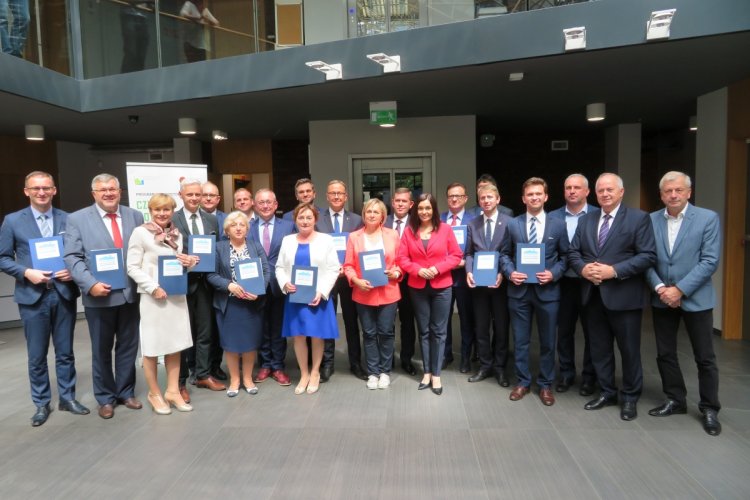 Na zdjęciu widać grupę osób, część z nich trzyma w rękach granatowe teczki z logo programu "Czyste Powietrze"