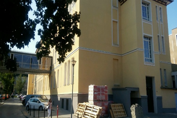 Budynek Uniwersyteckiego Centrum Klinicznego z zewnątrz, na ziemi leżą materiały budowlane, obok stoją samochody osobowe  