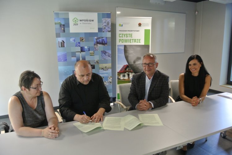 Przy stole siedzą cztery osoby i podpisują tysięczną umowę w ramach „Czystego Powietrza